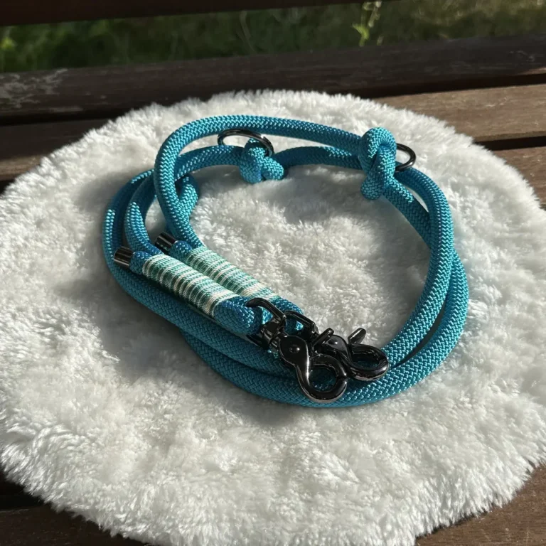 Eine Hundeleine aus blauem Tauseil mit blau-wißer Takelung auf einem weißen, runden und flauschigen Kissen, das auf einer Holzbank liegt.