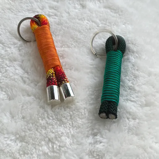 Zwei Schlüsselanhänger aus Tau in den Farben Orange und Schwarz-Türkis, die auf einem weißen Kissen liegen.