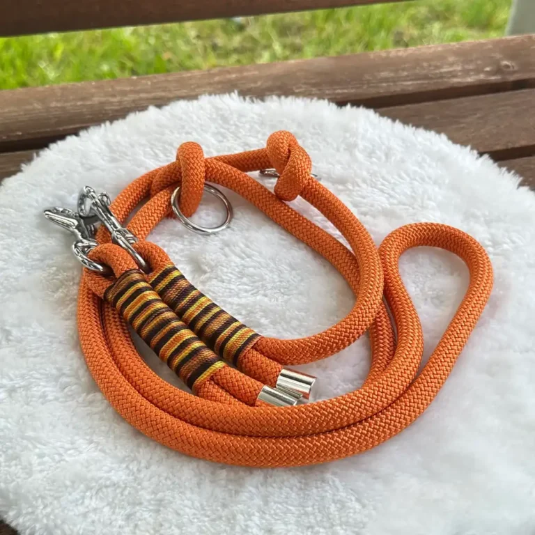 Eine Hundeleine aus orangenem Tauseil auf einem weißen, runden und flauschigen Kissen, das auf einer Holzbank liegt.