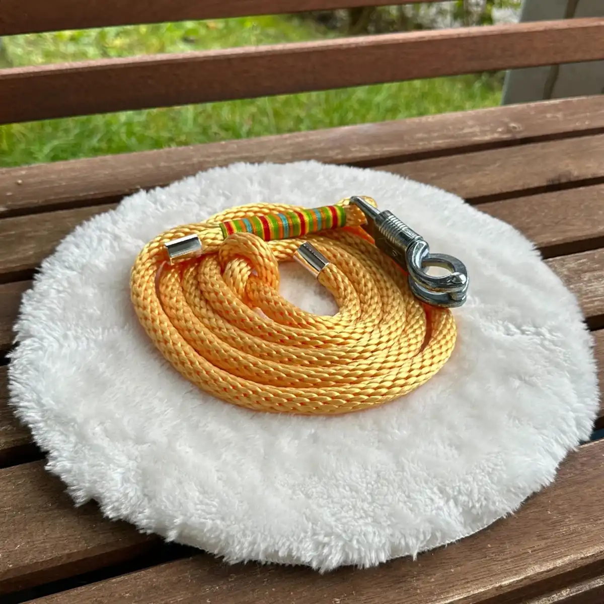 Ein Pferdeführstrick aus gelbem Tauseil auf einem weißen, runden und flauschigen Kissen, das auf einer Holzbank liegt.