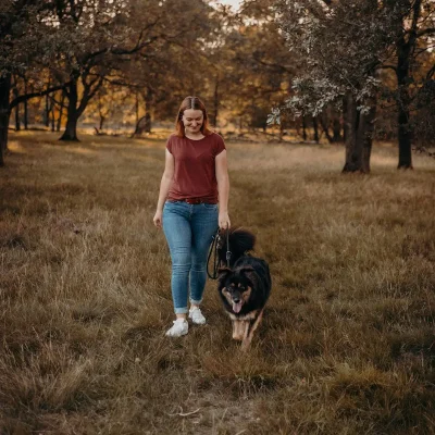 Eine junge Frau, die mit einem Hund an ihrer Seite lächelnd über eine Wiese läuft.