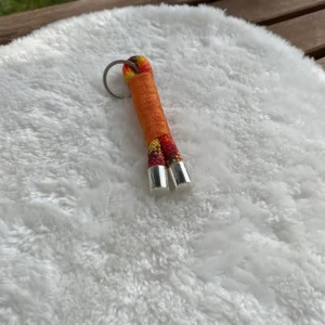 Ein orangener Schlüsselanhänger aus Tau mit silbernen Käppchen, der auf einem weißen Kissen liegt.